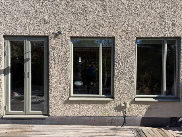 Putsad fasad med nya grågröna fönster med mittpost och en parfönsterdörr ut mot altanen